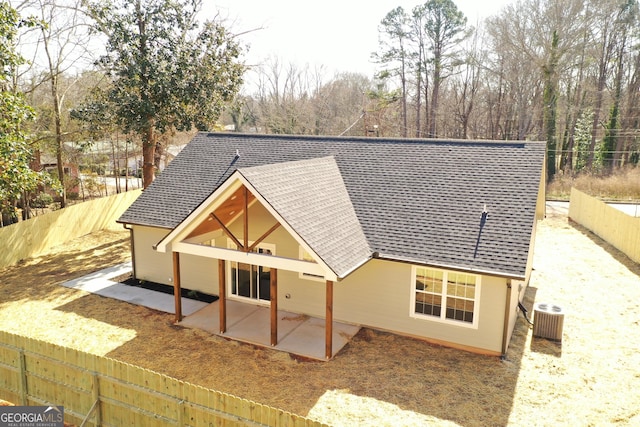 view of front of house featuring a shingled roof, cooling unit, a fenced backyard, and a patio