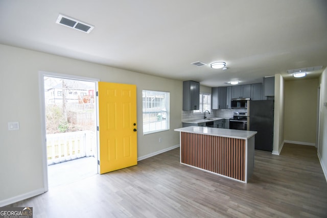 kitchen with gray cabinetry, light hardwood / wood-style flooring, appliances with stainless steel finishes, a kitchen island, and backsplash