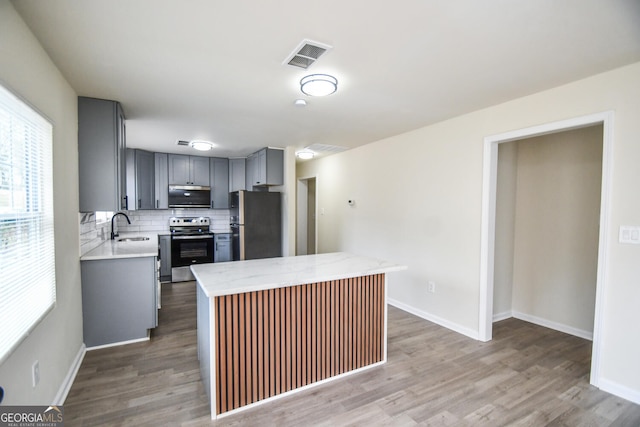 kitchen with sink, gray cabinets, appliances with stainless steel finishes, wood-type flooring, and decorative backsplash