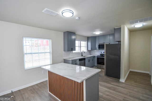 kitchen featuring sink, appliances with stainless steel finishes, light stone counters, a kitchen island, and decorative backsplash