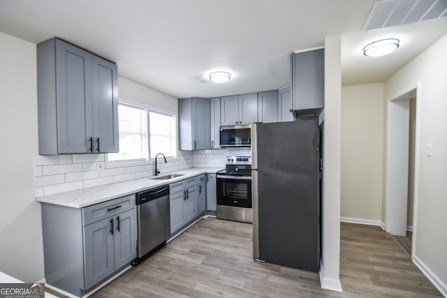 kitchen featuring sink, gray cabinets, appliances with stainless steel finishes, light stone counters, and decorative backsplash