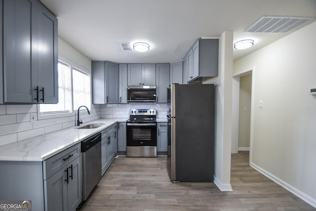 kitchen featuring sink, gray cabinetry, tasteful backsplash, light stone counters, and stainless steel appliances