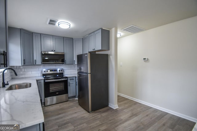 kitchen with sink, gray cabinets, appliances with stainless steel finishes, tasteful backsplash, and light stone countertops