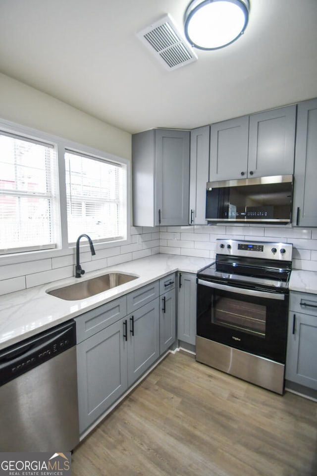 kitchen with sink, hardwood / wood-style flooring, gray cabinets, appliances with stainless steel finishes, and decorative backsplash