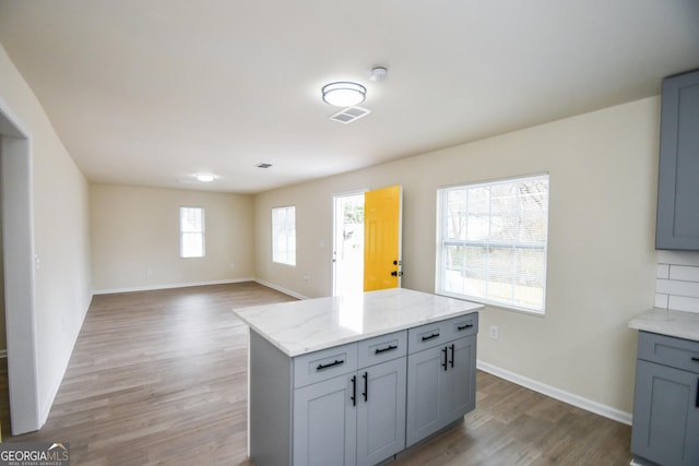 kitchen with hardwood / wood-style flooring, gray cabinets, a center island, and light stone countertops