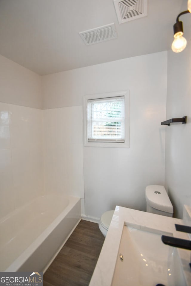 full bathroom featuring washtub / shower combination, wood-type flooring, toilet, and sink