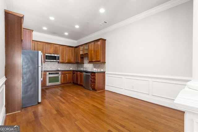 kitchen featuring decorative backsplash, ornamental molding, appliances with stainless steel finishes, and wood-type flooring