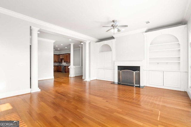 unfurnished living room featuring decorative columns, wood-type flooring, ceiling fan, crown molding, and built in shelves