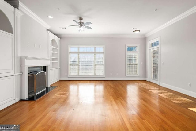 unfurnished living room featuring crown molding, ceiling fan, built in shelves, and light hardwood / wood-style floors