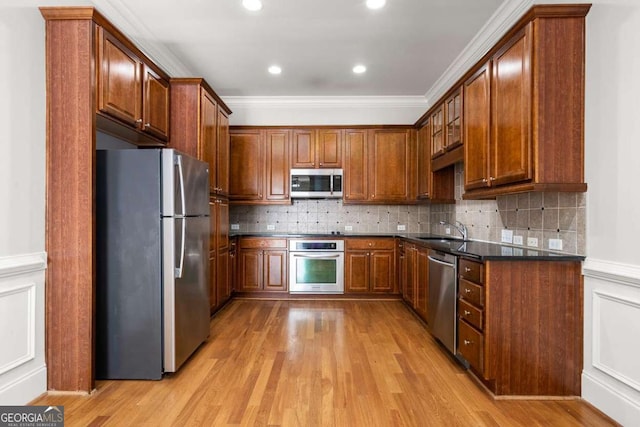 kitchen with stainless steel appliances, sink, light hardwood / wood-style flooring, and dark stone counters