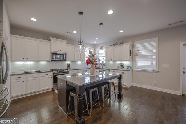 kitchen with a kitchen island, white cabinetry, appliances with stainless steel finishes, light stone countertops, and decorative light fixtures