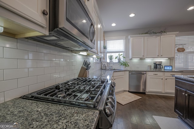 kitchen with white cabinets, appliances with stainless steel finishes, light stone counters, dark wood-type flooring, and a sink