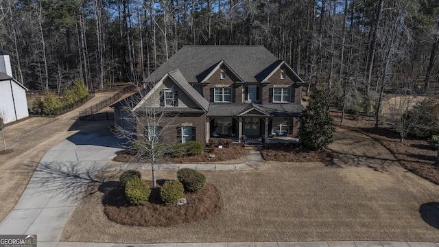 craftsman-style home with driveway, a shingled roof, a view of trees, and brick siding