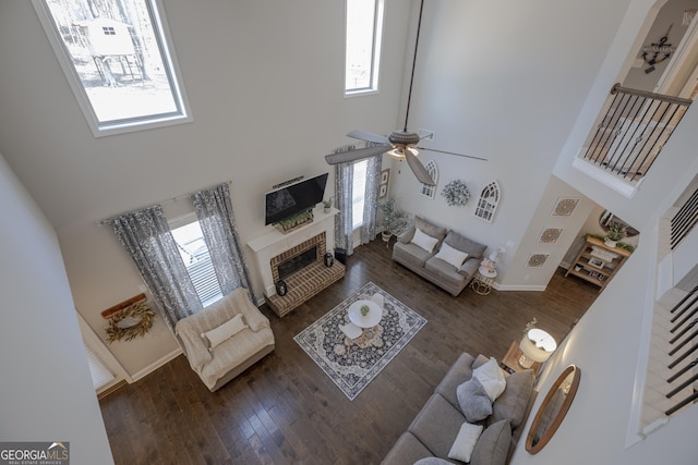 living room with a healthy amount of sunlight, a brick fireplace, a high ceiling, and dark wood-style flooring