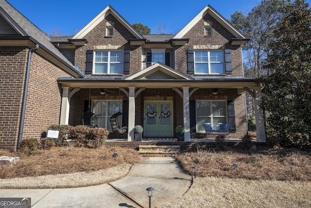 view of front of house featuring covered porch, brick siding, and french doors