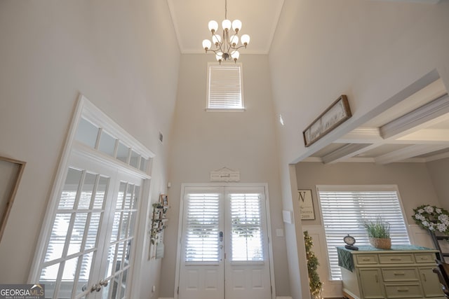 foyer entrance with ornamental molding, french doors, beamed ceiling, and a chandelier