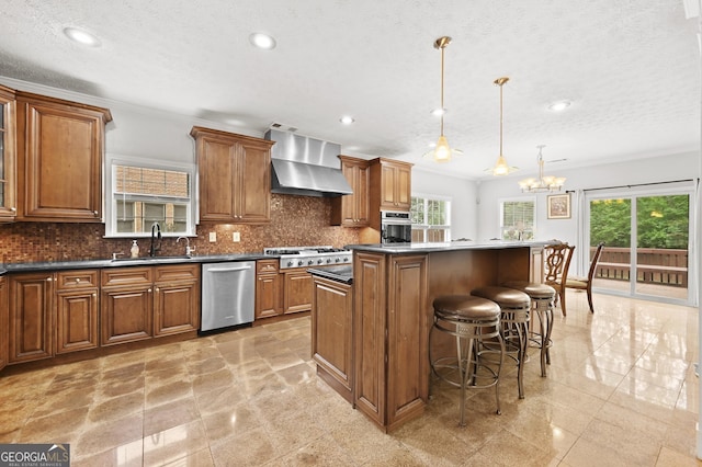 kitchen featuring wall chimney exhaust hood, sink, a center island, appliances with stainless steel finishes, and pendant lighting