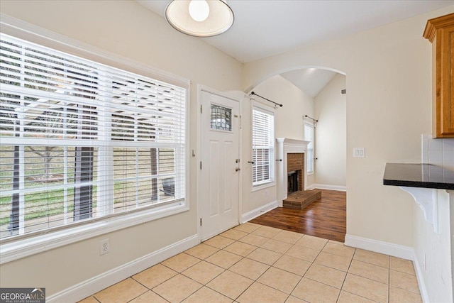 entryway with a fireplace, vaulted ceiling, and light tile patterned floors