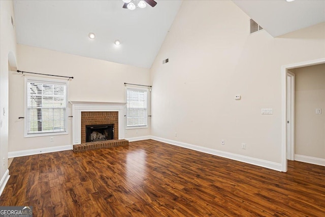 unfurnished living room featuring high vaulted ceiling, a healthy amount of sunlight, dark hardwood / wood-style flooring, and a brick fireplace