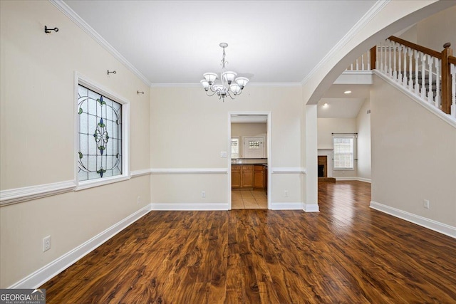 unfurnished dining area featuring wood-type flooring, a brick fireplace, ornamental molding, and an inviting chandelier