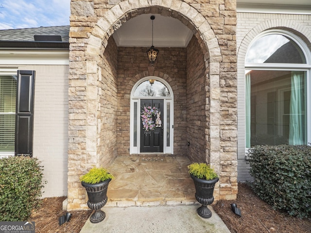 doorway to property featuring stone siding, brick siding, and roof with shingles