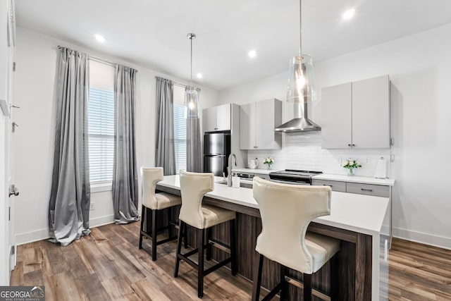 kitchen featuring wall chimney exhaust hood, a kitchen bar, hanging light fixtures, appliances with stainless steel finishes, and backsplash