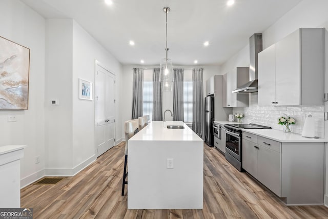 kitchen featuring stainless steel appliances, pendant lighting, gray cabinetry, and wall chimney exhaust hood