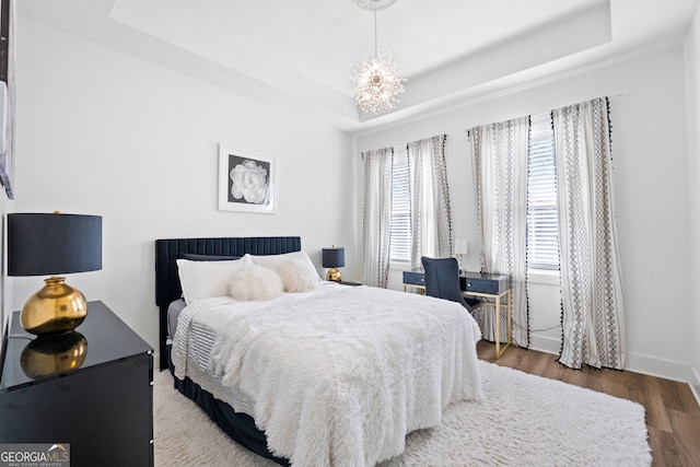 bedroom with a chandelier, a tray ceiling, baseboards, and wood finished floors