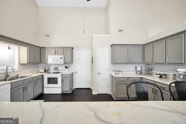 kitchen featuring sink, gray cabinetry, light stone counters, pendant lighting, and white appliances