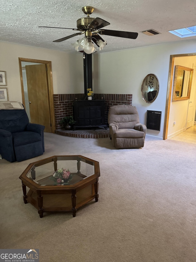 living room with ceiling fan, a skylight, a textured ceiling, light colored carpet, and a wood stove