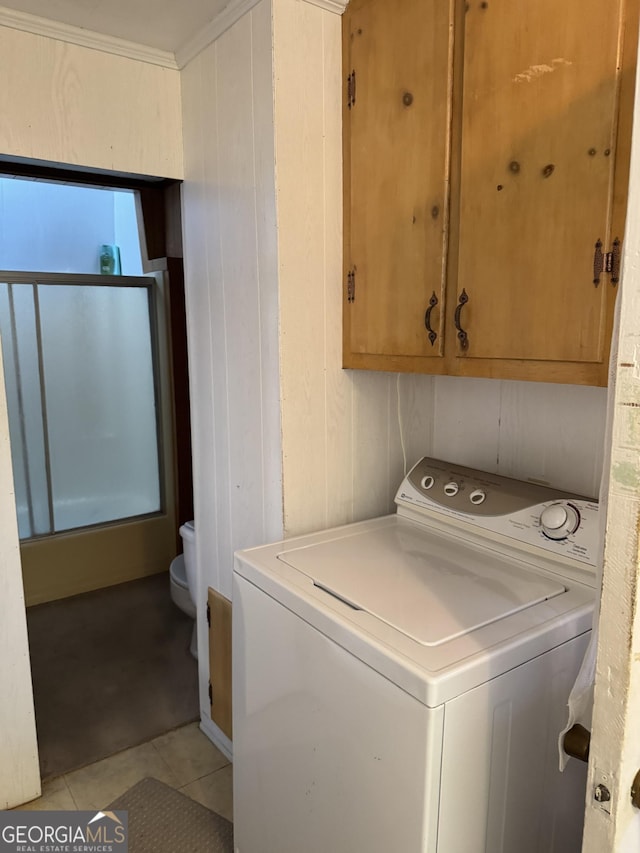 laundry area with light tile patterned floors, washer / dryer, cabinets, and wood walls