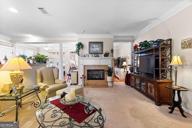 carpeted living room featuring decorative columns, a tile fireplace, ornamental molding, and ceiling fan