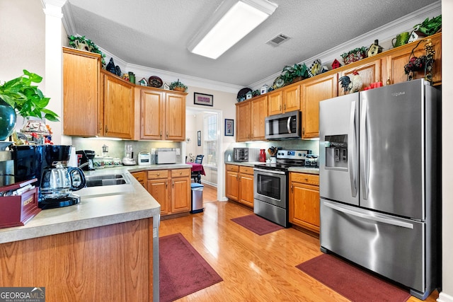 kitchen featuring ornamental molding, stainless steel appliances, a textured ceiling, and light wood-type flooring