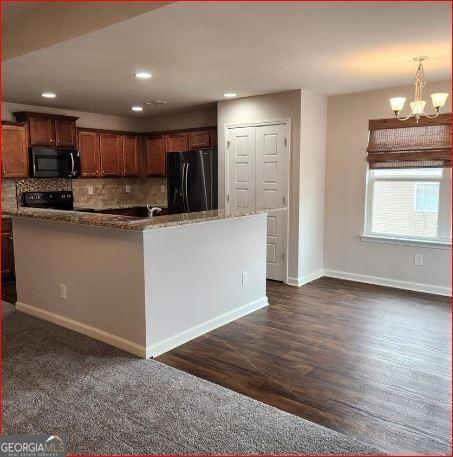 kitchen featuring pendant lighting, backsplash, stove, a notable chandelier, and black fridge