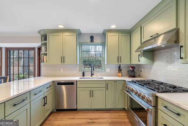 kitchen with sink, range hood, stainless steel appliances, light stone countertops, and green cabinetry