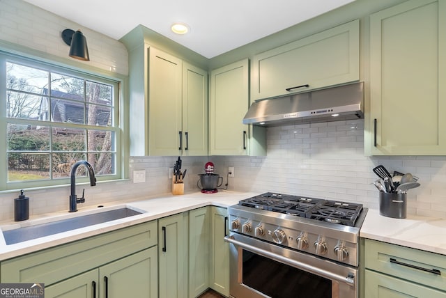 kitchen featuring sink, light stone counters, green cabinetry, stainless steel stove, and backsplash