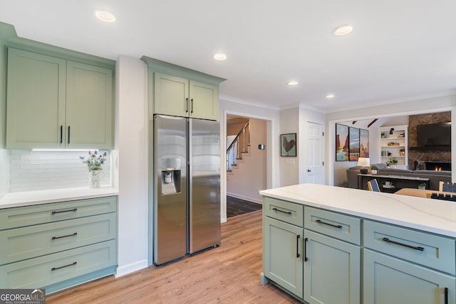 kitchen featuring crown molding, stainless steel refrigerator with ice dispenser, green cabinetry, decorative backsplash, and light wood-type flooring