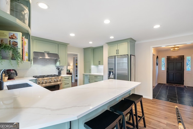 kitchen with sink, tasteful backsplash, appliances with stainless steel finishes, green cabinets, and light stone countertops