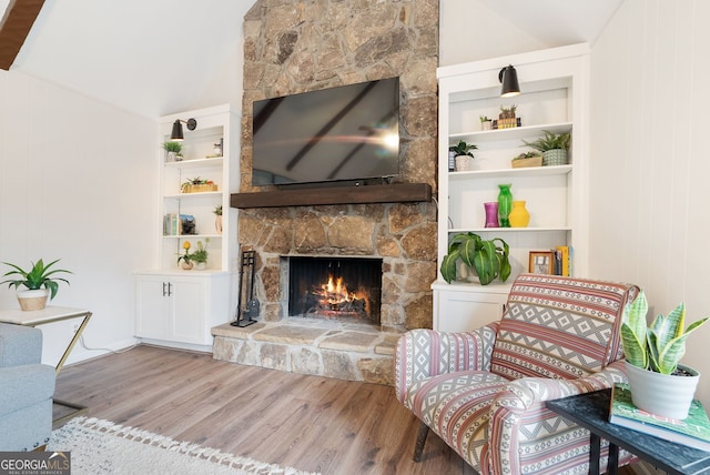 living room featuring wooden walls, built in shelves, a stone fireplace, vaulted ceiling, and light wood-type flooring