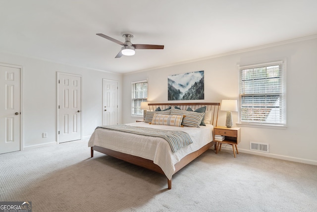 carpeted bedroom featuring multiple windows, crown molding, two closets, and ceiling fan