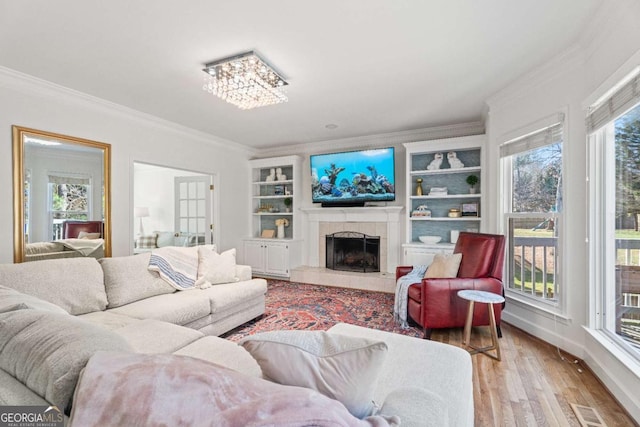 living room featuring ornamental molding, a tiled fireplace, built in features, and light wood-type flooring