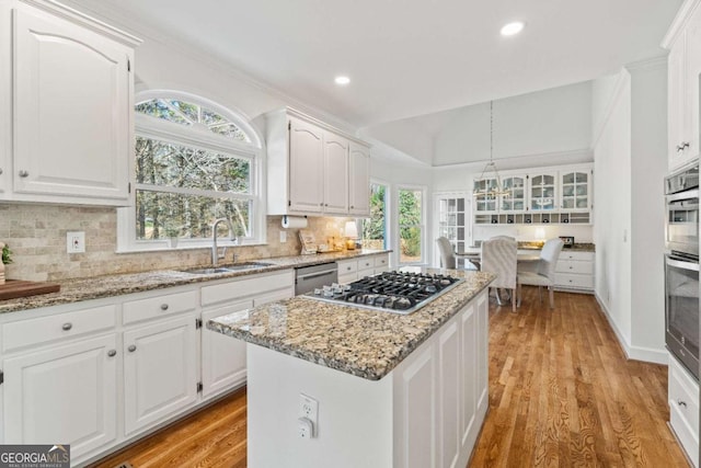 kitchen with appliances with stainless steel finishes, decorative light fixtures, white cabinetry, sink, and a center island