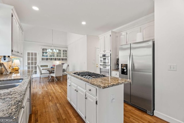 kitchen featuring appliances with stainless steel finishes, white cabinetry, hardwood / wood-style floors, a center island, and light stone counters