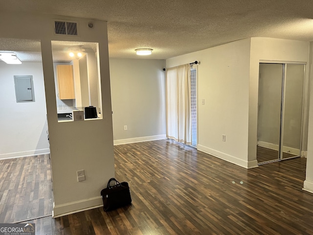 unfurnished living room featuring dark hardwood / wood-style floors, electric panel, and a textured ceiling