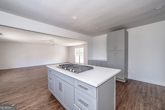 kitchen with gray cabinetry, dark hardwood / wood-style flooring, stainless steel gas stovetop, and a kitchen island