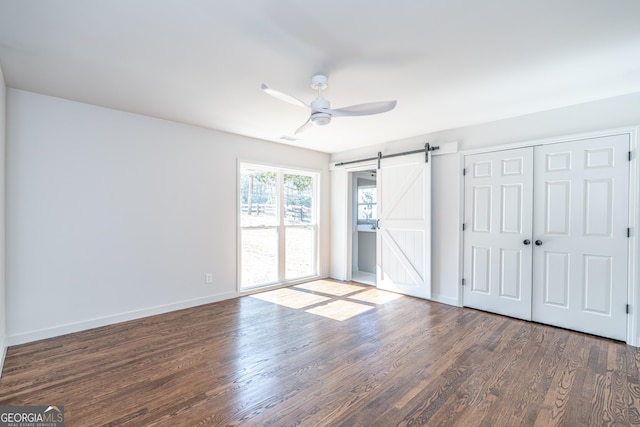 interior space with dark hardwood / wood-style flooring, a barn door, and ceiling fan