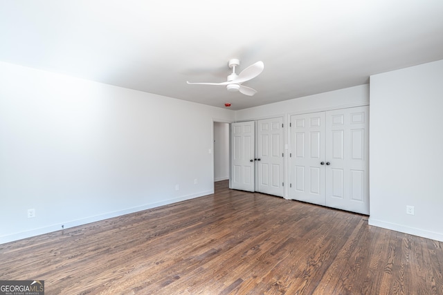 unfurnished bedroom with ceiling fan, dark hardwood / wood-style flooring, and two closets