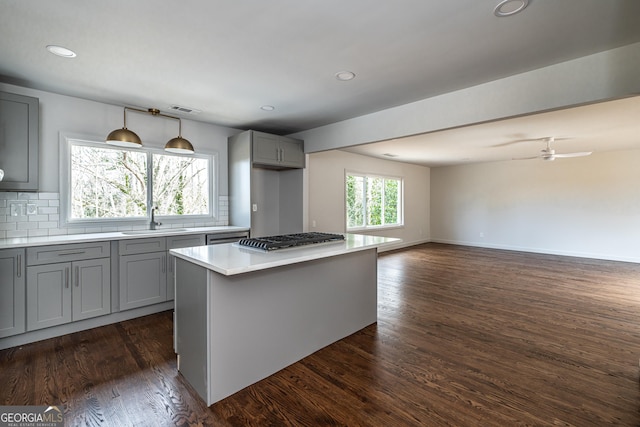 kitchen with sink, gray cabinetry, dark hardwood / wood-style floors, stainless steel gas cooktop, and a kitchen island