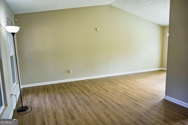 empty room featuring lofted ceiling, dark wood-type flooring, and a textured ceiling