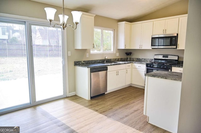 kitchen with vaulted ceiling, appliances with stainless steel finishes, pendant lighting, white cabinetry, and light hardwood / wood-style flooring